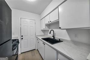 kitchen with range, white cabinets, light wood-style flooring, freestanding refrigerator, and a sink