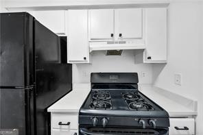 kitchen with light countertops, under cabinet range hood, black appliances, and white cabinetry