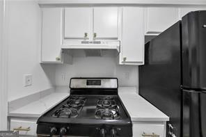 kitchen with under cabinet range hood, stainless steel range with gas cooktop, white cabinetry, and light countertops