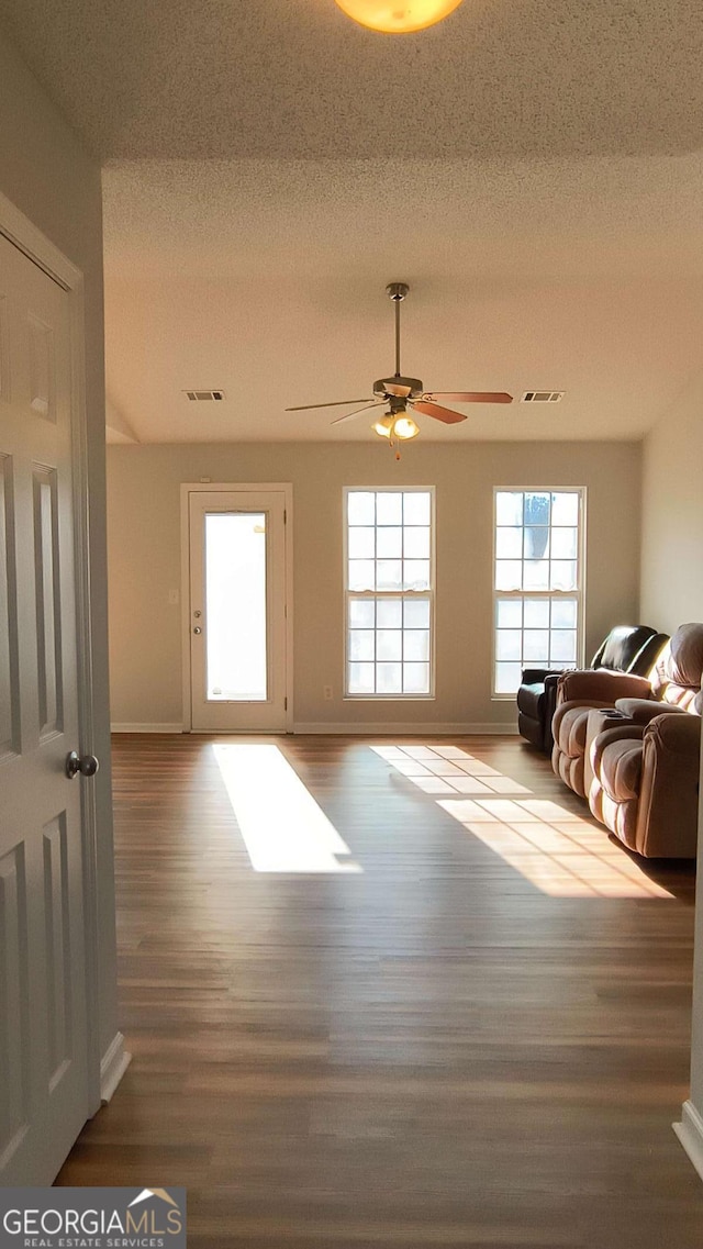 unfurnished living room featuring a textured ceiling, wood finished floors, visible vents, baseboards, and a ceiling fan