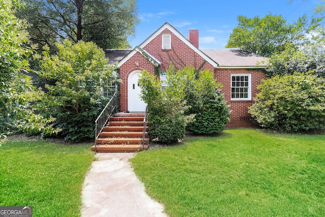 view of front facade featuring entry steps, brick siding, a chimney, and a front lawn