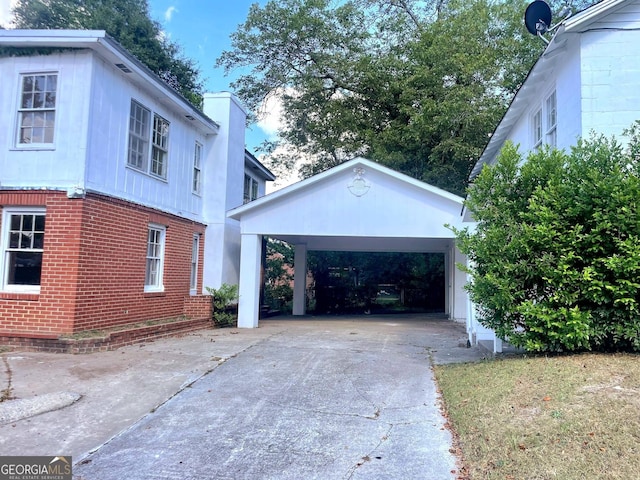 view of side of home with a carport, a chimney, concrete driveway, and brick siding