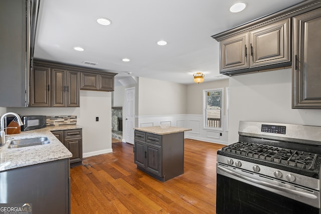 kitchen with dark wood-style flooring, visible vents, stainless steel range with gas stovetop, a sink, and light stone countertops