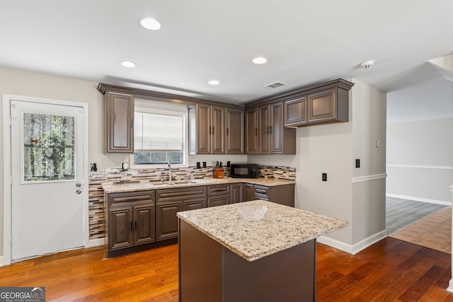 kitchen featuring dark wood-style floors, a sink, light stone countertops, and a center island