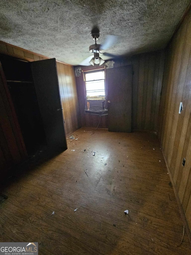 interior space with a textured ceiling, ceiling fan, dark wood-type flooring, and wooden walls