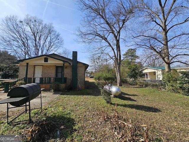 view of property exterior with brick siding, a chimney, a porch, and a lawn