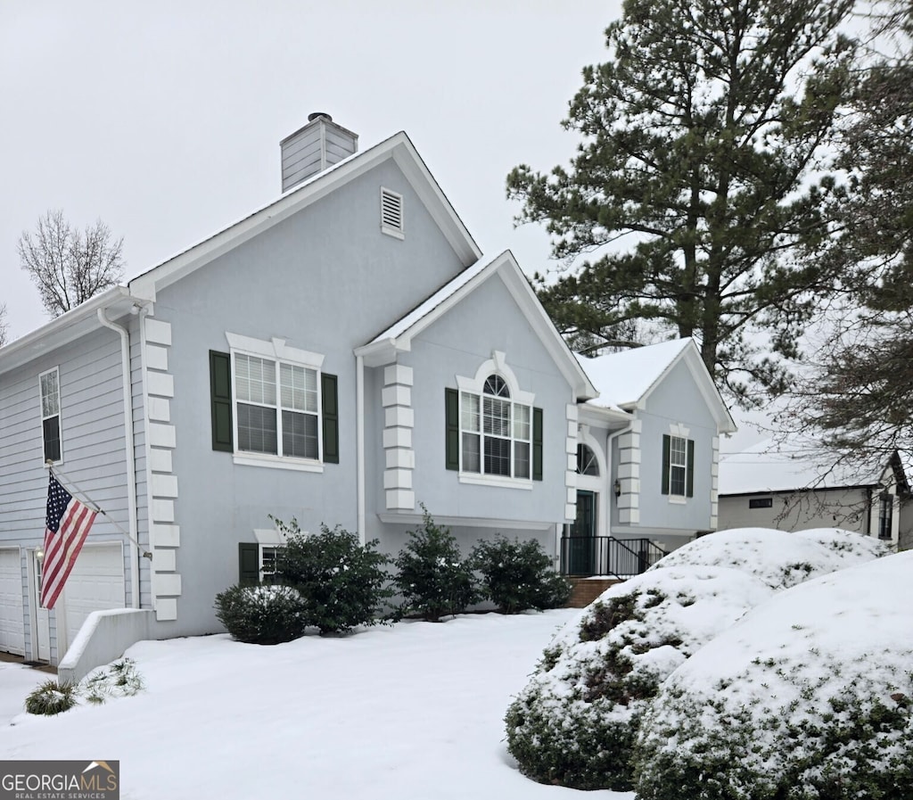 view of front of home with an attached garage, a chimney, and stucco siding