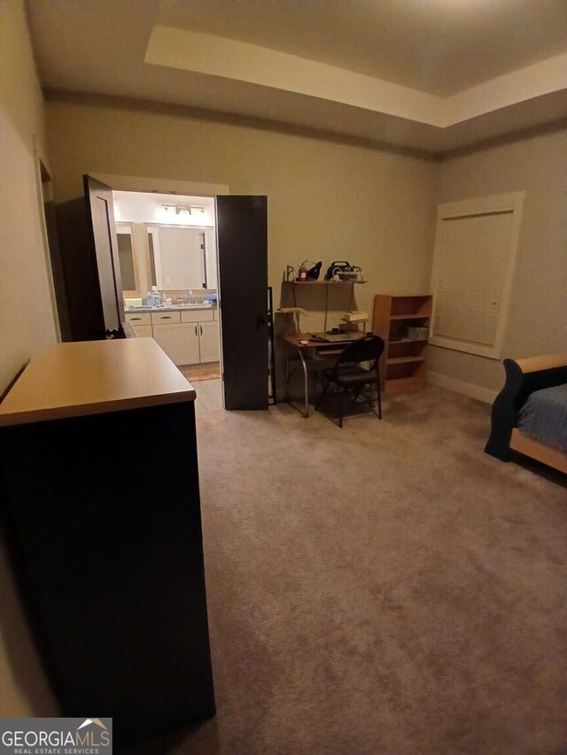 bedroom with light carpet, ensuite bath, and a raised ceiling