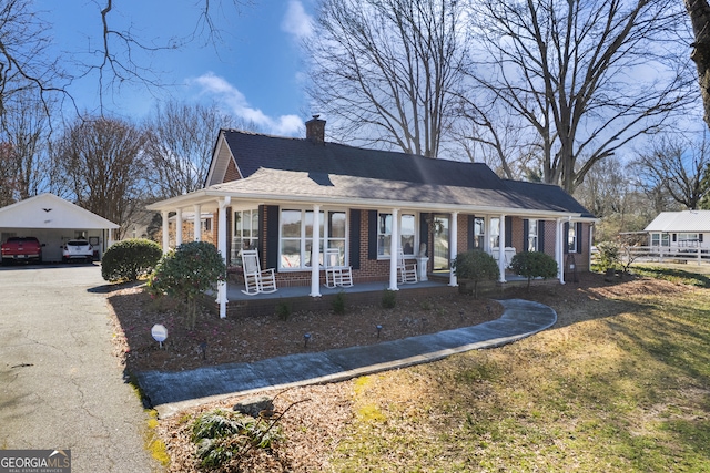 view of front facade with covered porch, brick siding, a chimney, and aphalt driveway