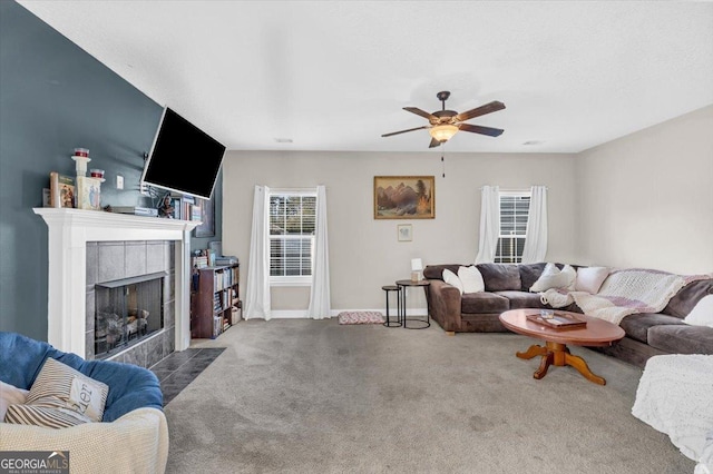 carpeted living area with ceiling fan, a tile fireplace, and baseboards