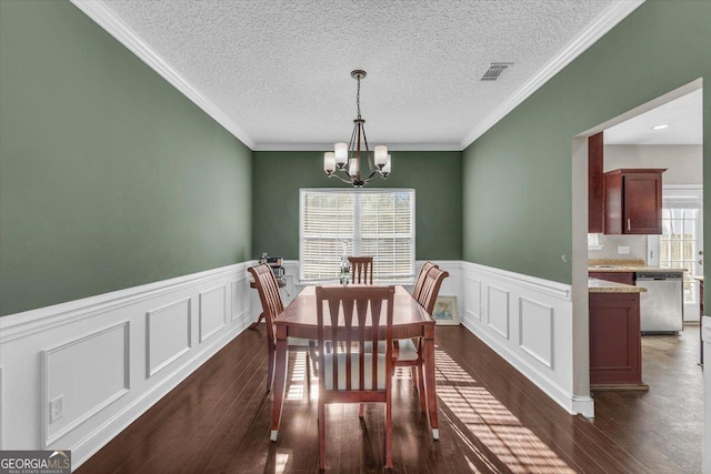 dining area featuring dark wood-style flooring, visible vents, an inviting chandelier, ornamental molding, and wainscoting