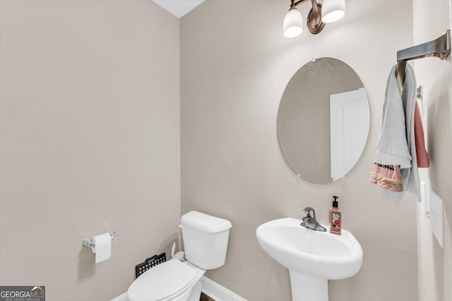 half bathroom featuring toilet, baseboards, and a sink