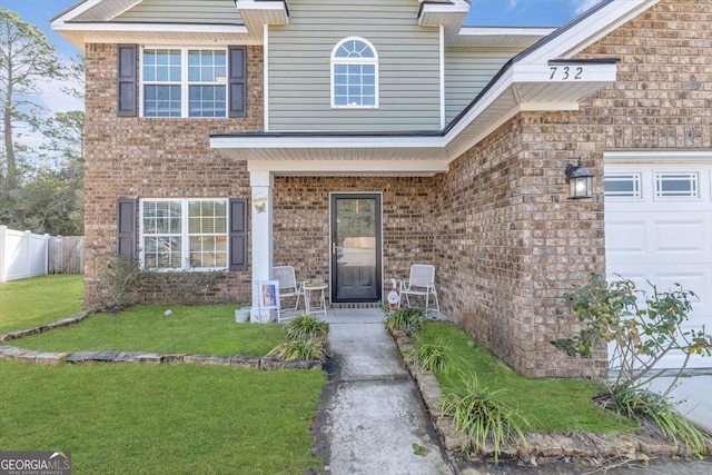 doorway to property with a garage, fence, a lawn, and brick siding