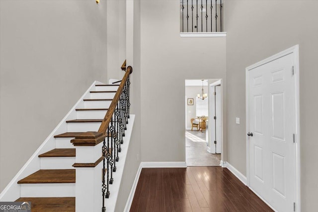 staircase with a high ceiling, a notable chandelier, baseboards, and wood finished floors