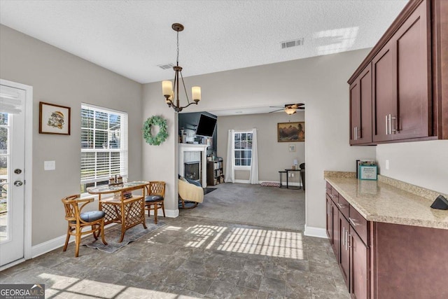 dining space featuring baseboards, visible vents, a textured ceiling, a fireplace, and ceiling fan with notable chandelier