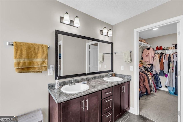 full bathroom with double vanity, a textured ceiling, a spacious closet, and a sink