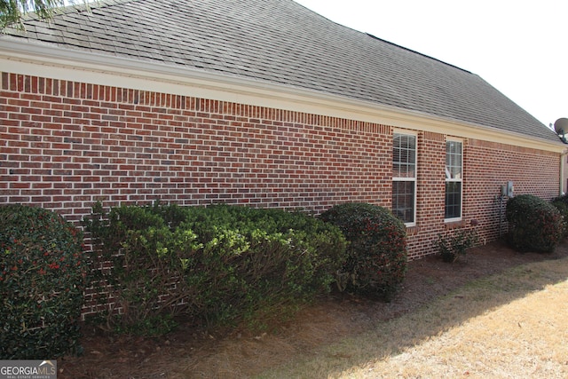 view of side of property with a shingled roof and brick siding