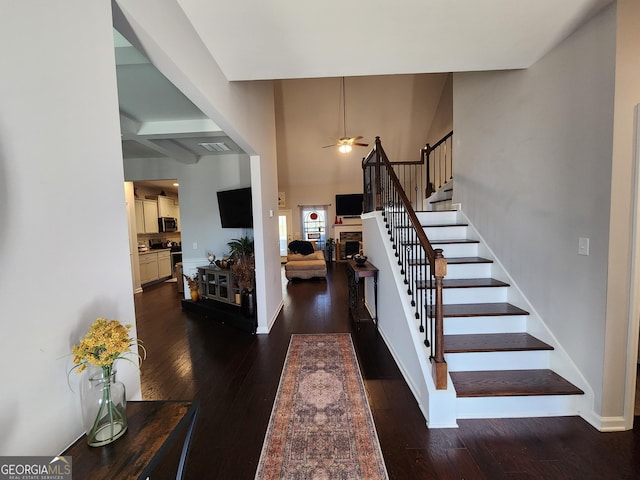 entryway featuring a stone fireplace, dark wood-type flooring, a ceiling fan, baseboards, and stairway