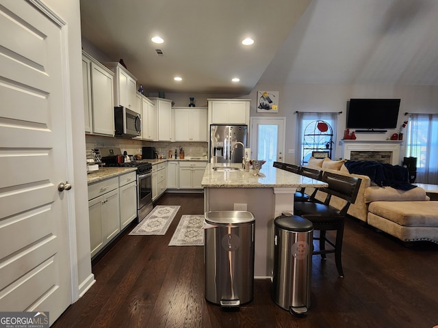 kitchen featuring a center island with sink, appliances with stainless steel finishes, open floor plan, and light stone counters