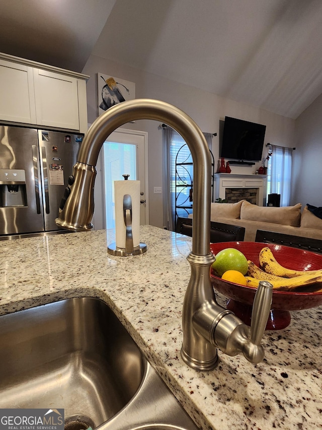 room details featuring light stone counters, a fireplace, a sink, white cabinetry, and stainless steel fridge with ice dispenser