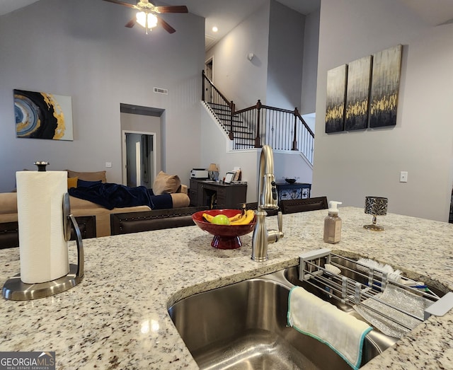 kitchen with visible vents, a ceiling fan, light stone counters, open floor plan, and a sink