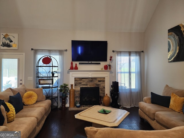 living area featuring lofted ceiling, dark wood finished floors, and a stone fireplace