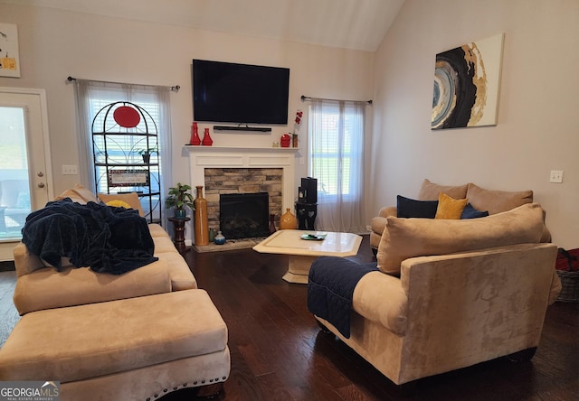 living room featuring vaulted ceiling, dark wood-type flooring, and a stone fireplace