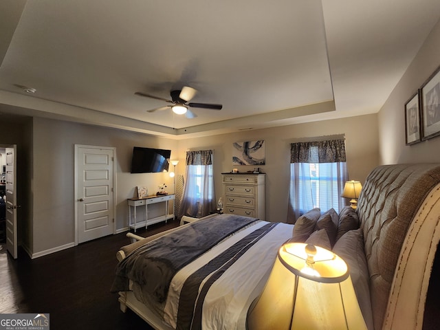 bedroom with a tray ceiling, dark wood finished floors, a ceiling fan, and baseboards