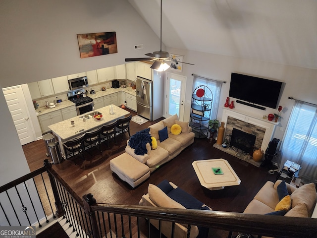 living area featuring high vaulted ceiling, a stone fireplace, visible vents, a ceiling fan, and dark wood-style floors