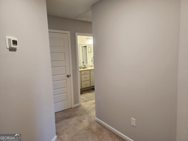 hallway with light carpet, attic access, and baseboards