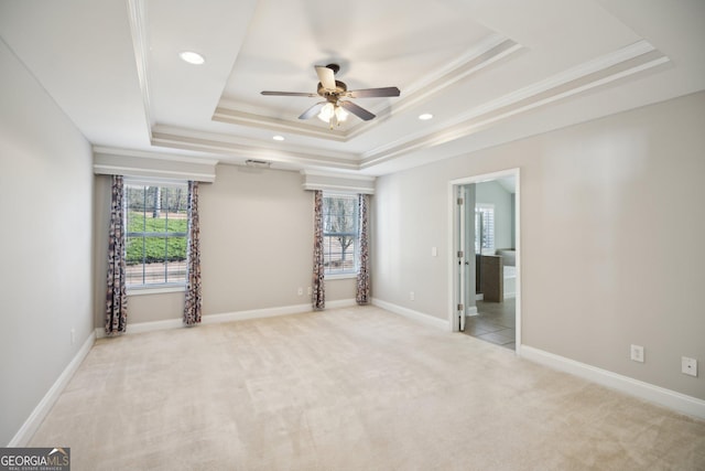 unfurnished bedroom with a tray ceiling, light carpet, crown molding, and multiple windows