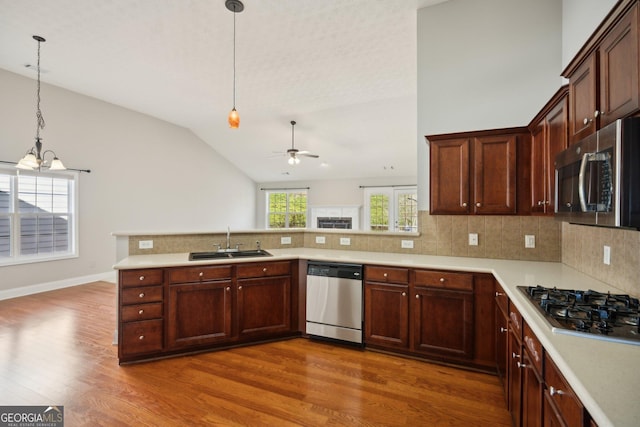 kitchen with a peninsula, a sink, light countertops, appliances with stainless steel finishes, and decorative light fixtures