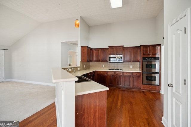 kitchen with a peninsula, a sink, light countertops, appliances with stainless steel finishes, and pendant lighting