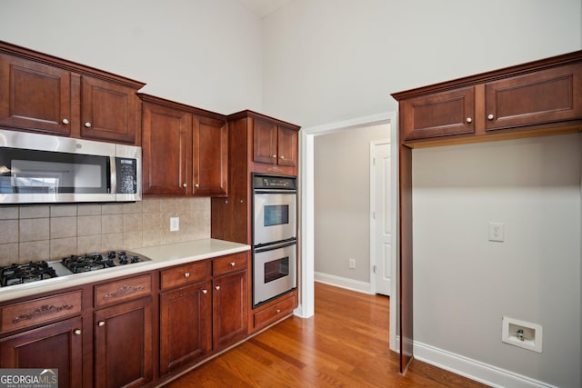 kitchen with a towering ceiling, appliances with stainless steel finishes, wood finished floors, light countertops, and backsplash