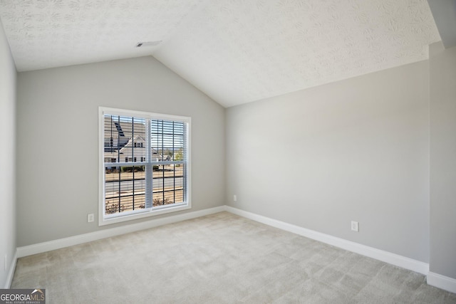 spare room with light colored carpet, visible vents, vaulted ceiling, a textured ceiling, and baseboards