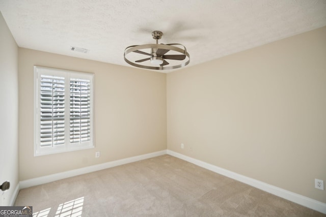 unfurnished room with light colored carpet, visible vents, a ceiling fan, a textured ceiling, and baseboards