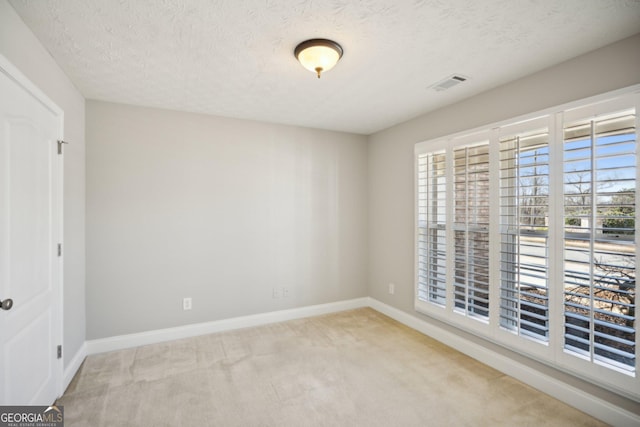 empty room with baseboards, a textured ceiling, visible vents, and light colored carpet