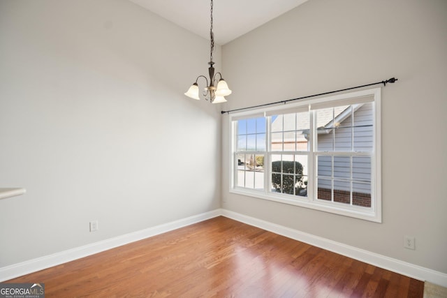 unfurnished dining area with lofted ceiling, a notable chandelier, baseboards, and wood finished floors