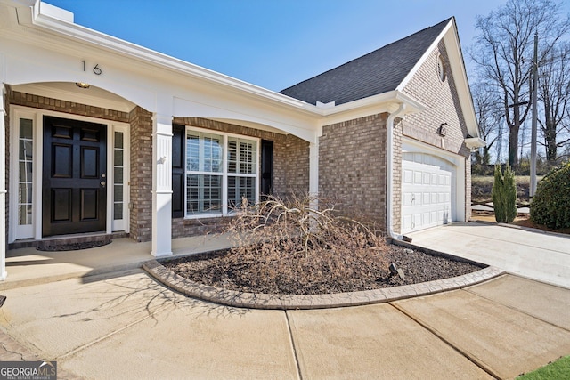 entrance to property featuring brick siding, a shingled roof, a porch, a garage, and driveway