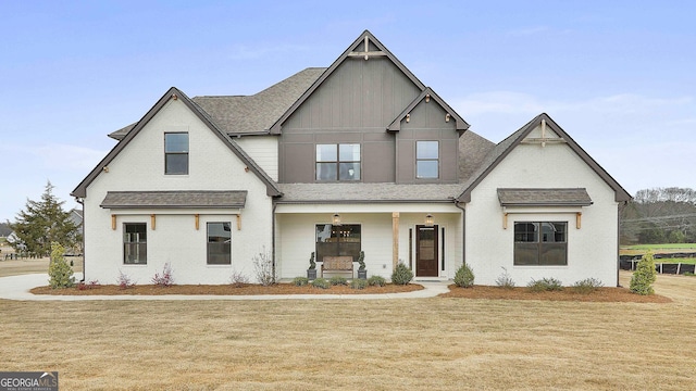 view of front of house featuring roof with shingles, a front yard, a porch, board and batten siding, and brick siding