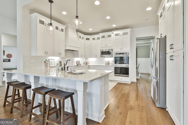 kitchen with appliances with stainless steel finishes, glass insert cabinets, a peninsula, hanging light fixtures, and white cabinetry