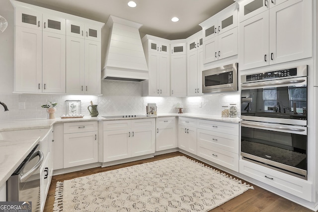 kitchen featuring stainless steel appliances, wall chimney range hood, glass insert cabinets, and white cabinetry