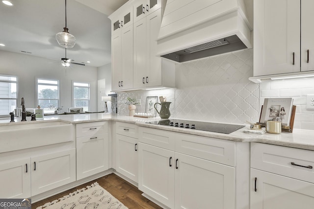 kitchen featuring light stone counters, black electric stovetop, custom range hood, glass insert cabinets, and a sink