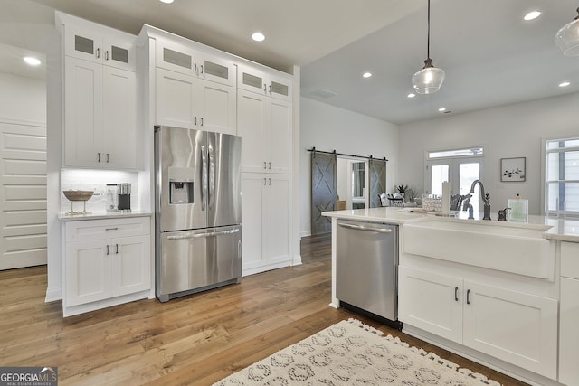 kitchen featuring stainless steel appliances, light countertops, a barn door, glass insert cabinets, and white cabinets