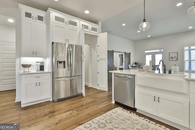 kitchen featuring a barn door, white cabinetry, light countertops, appliances with stainless steel finishes, and glass insert cabinets