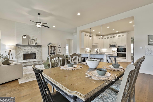 dining space with baseboards, ceiling fan, a stone fireplace, light wood-type flooring, and recessed lighting