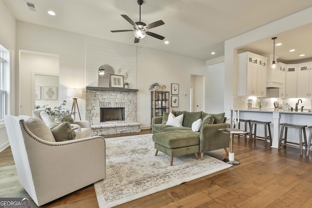 living area featuring a stone fireplace, recessed lighting, visible vents, a ceiling fan, and dark wood-style floors