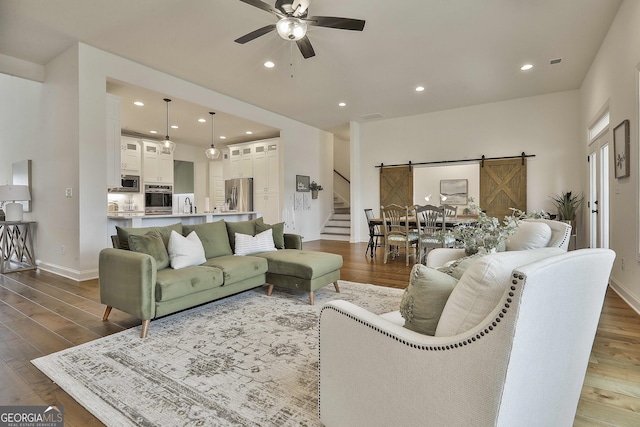 living room featuring ceiling fan, a barn door, recessed lighting, stairs, and dark wood-style floors