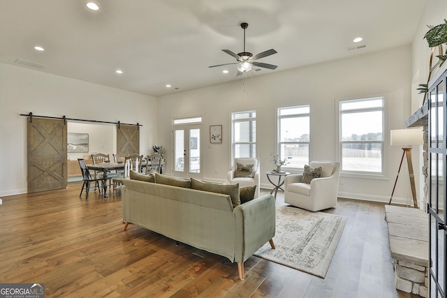 living area featuring a barn door, recessed lighting, wood finished floors, visible vents, and french doors