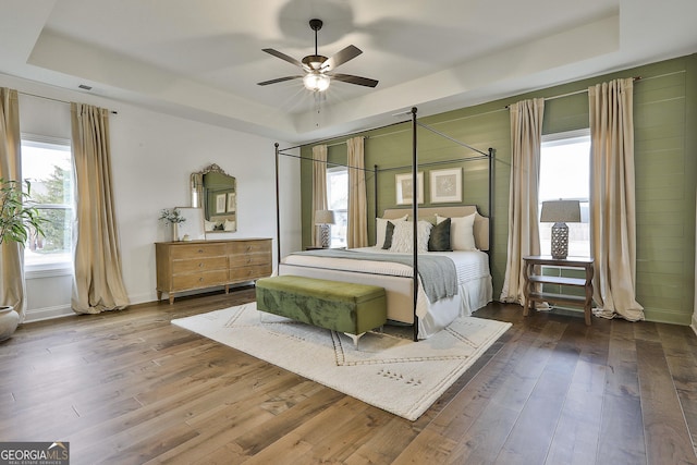 bedroom featuring a ceiling fan, a tray ceiling, baseboards, and wood finished floors